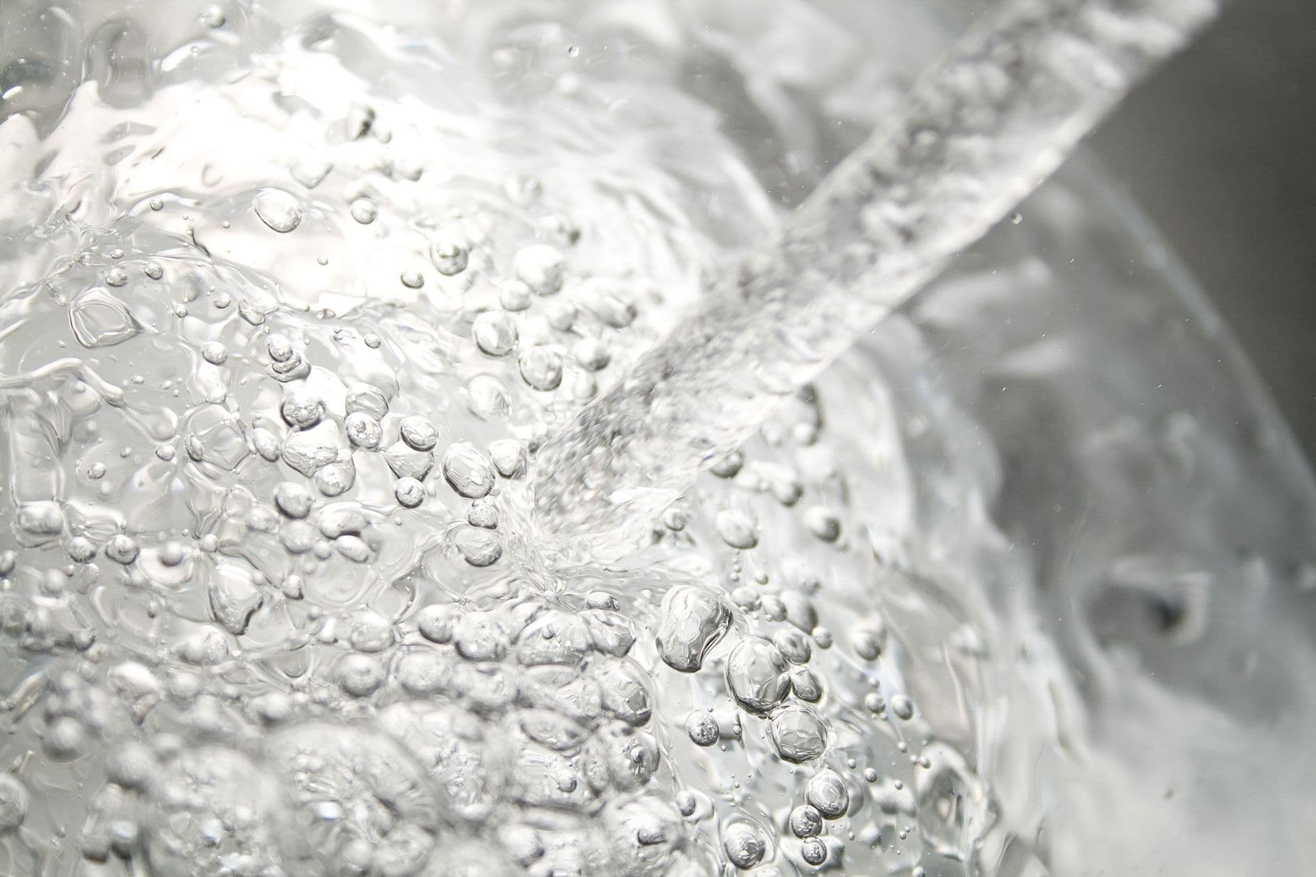 Close-up of a stream of water with swirling bubbles beneath the surface, creating a dynamic and refreshing visual effect.
